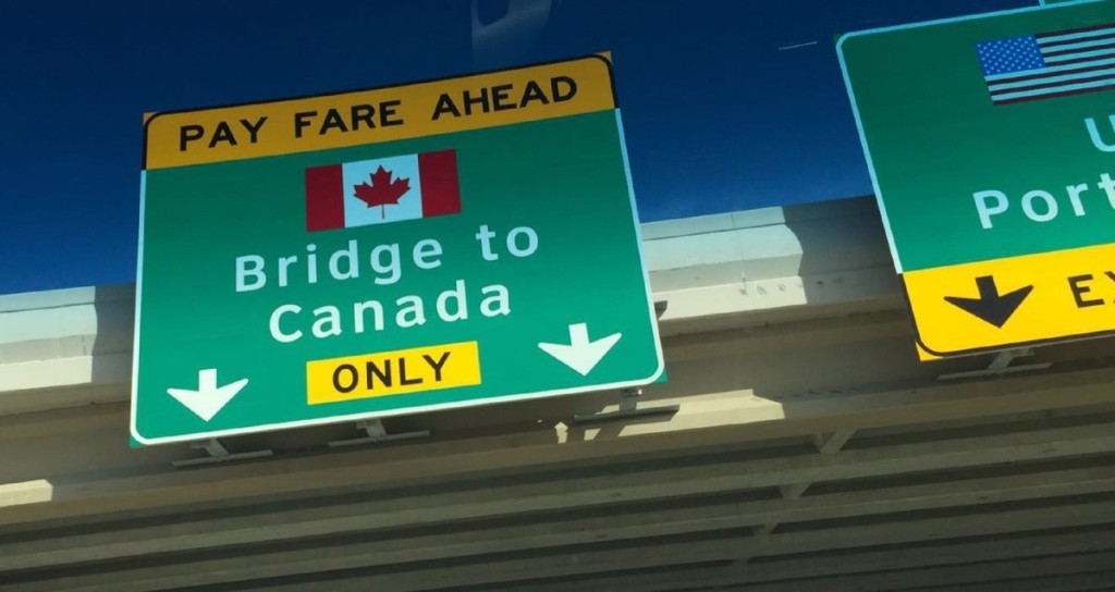 A sign posted on an overpass with that says 'Pay fare ahead' and pointing toward a bridge to Canada.